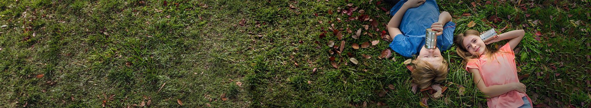 Kids lying in the grass using tin cans as communication instruments
