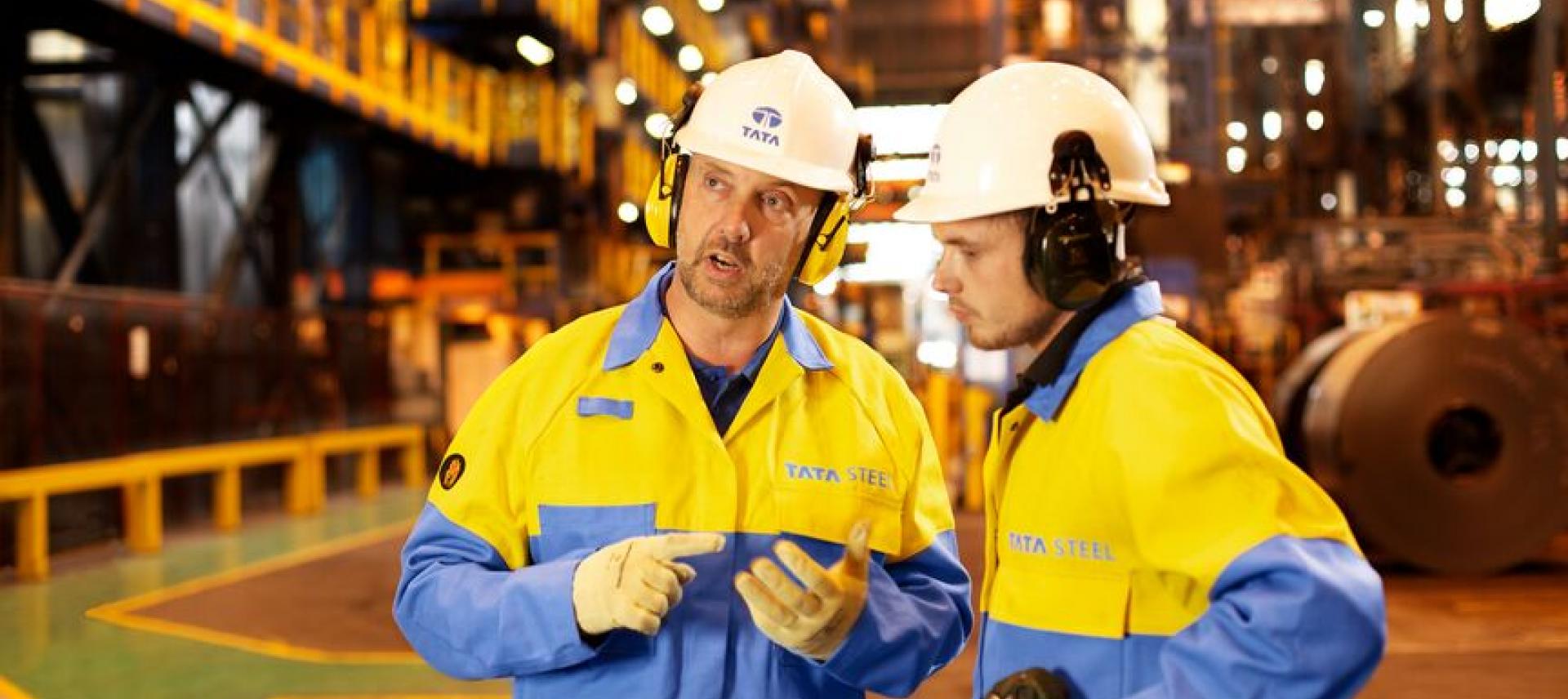 Tata Steel workers in a manufacturing environment, wearing protective equipment, having a discussion Tata Steel workers in a manufacturing environment, wearing protective equipment, having a discussion