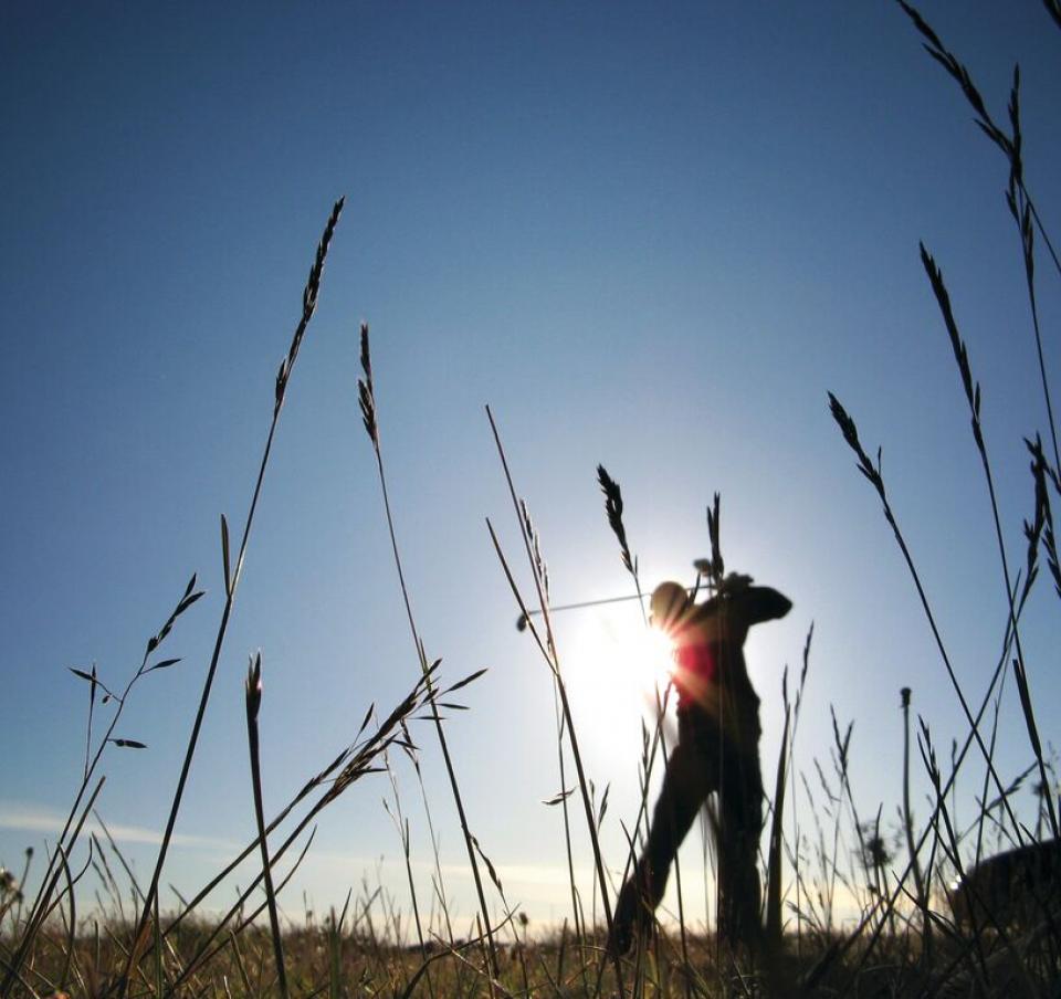 Silhouette of man playing golf against backdrop of sunshine and blue sky Silhouette of man playing golf against backdrop of sunshine and blue sky
