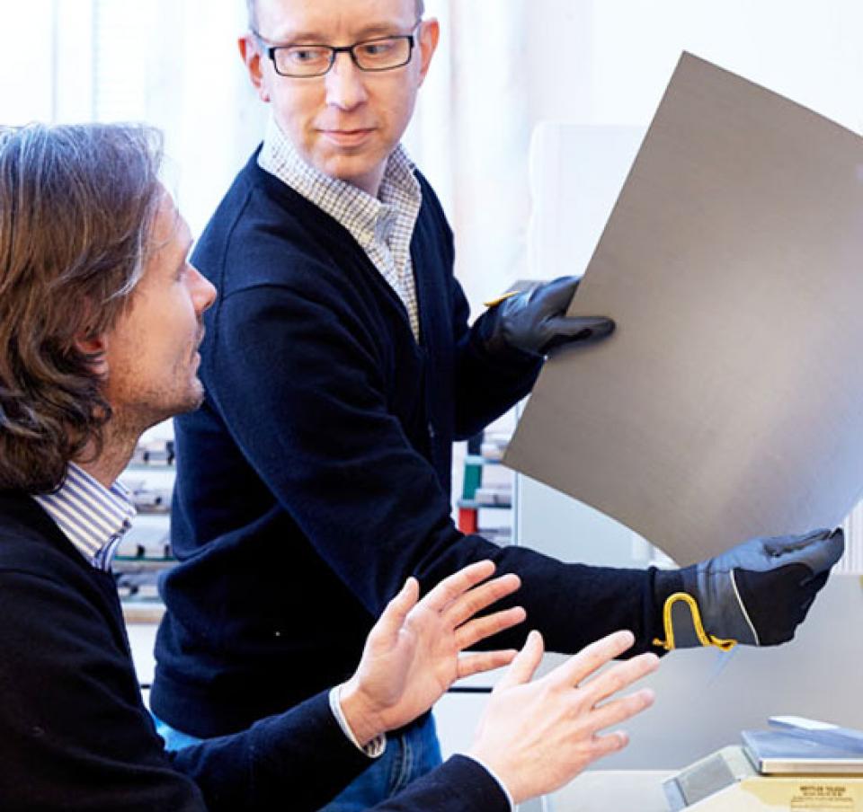 Two men, one holding a panel, having a discussion Two men, one holding a panel, having a discussion