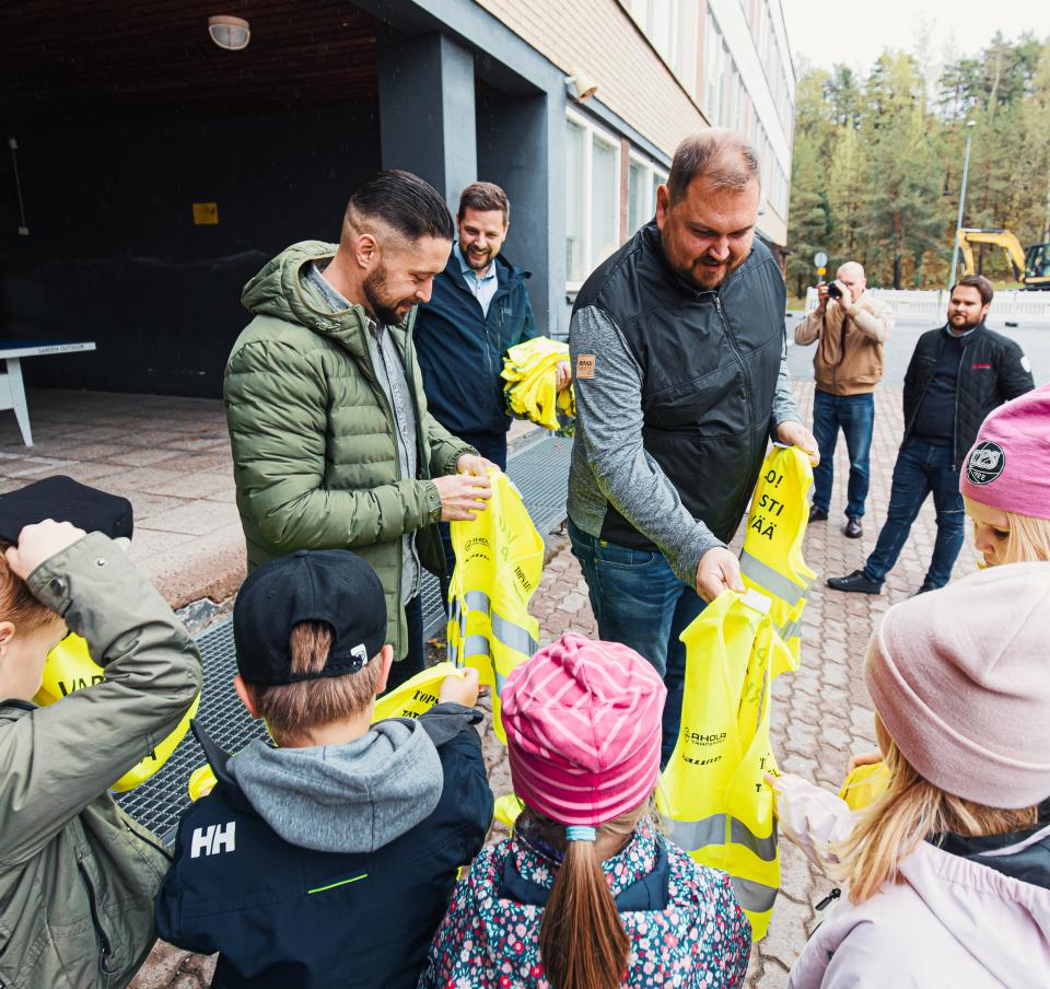 Children being handed high visibility vests to keep then safe when crossing the road.
