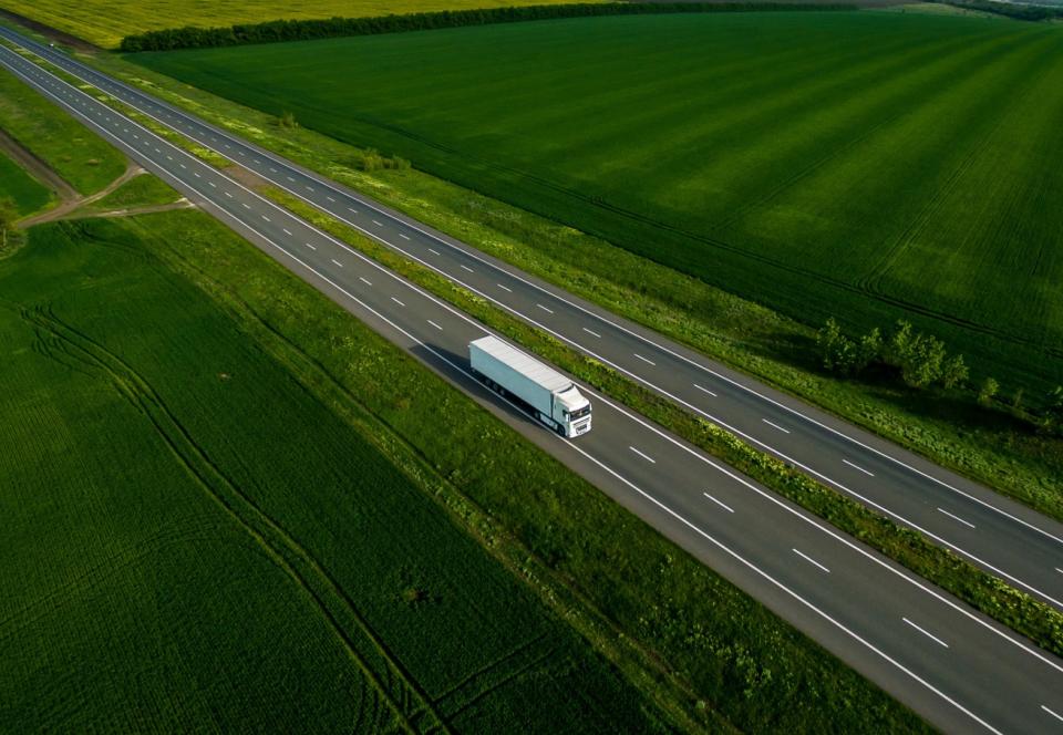 White truck driving on highway through green fields