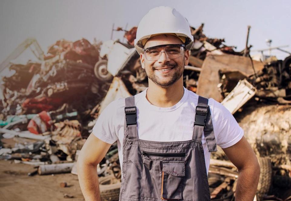 Man with working clothes and hat in front of steel scrap pile