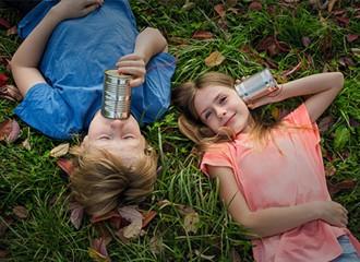 Boy and girl lying in grass communicating through steel cans